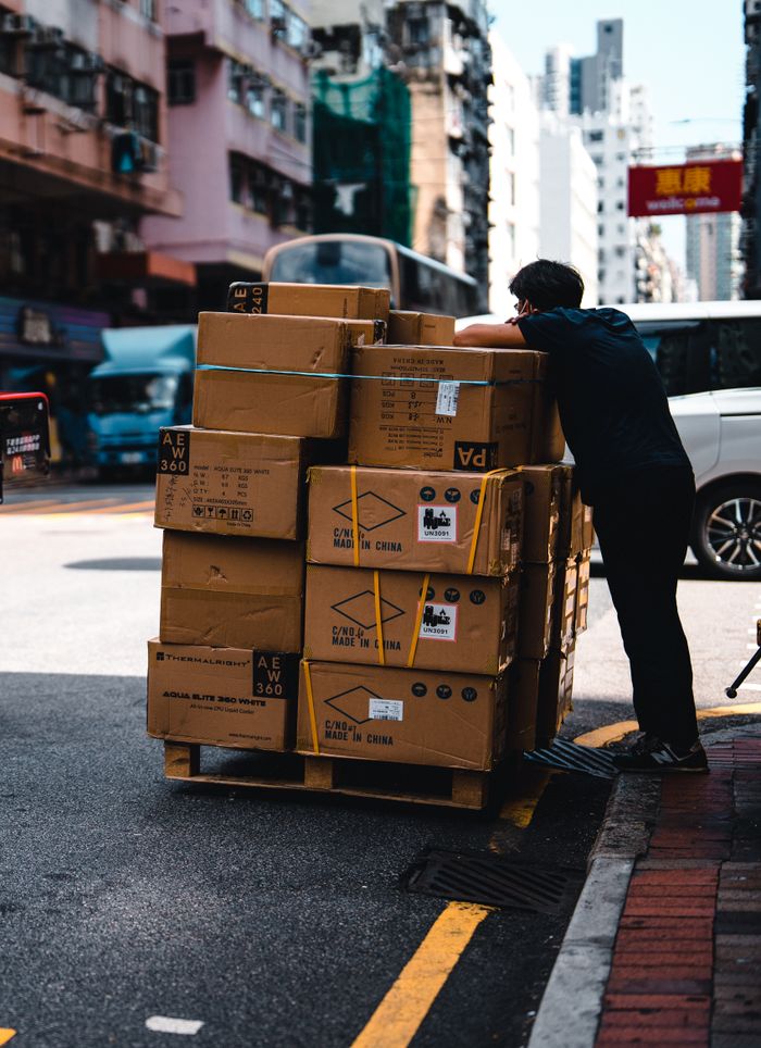 vision Man handling stacked boxes on a pallet in busy urban street scene.