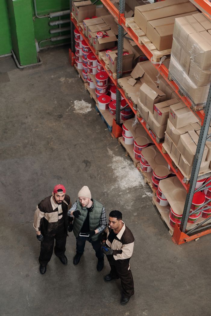 our-story Workers in a warehouse discussing logistics near shelves filled with packages and products.