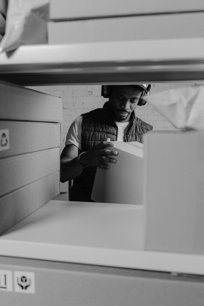 services-01 A courier wearing headphones organizes cardboard boxes on a shelf inside a warehouse.