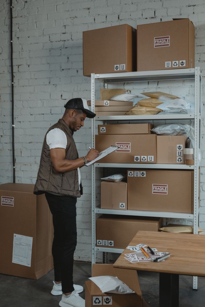 journey-02 A delivery worker noting shipping details on a clipboard by shelves of packages.
