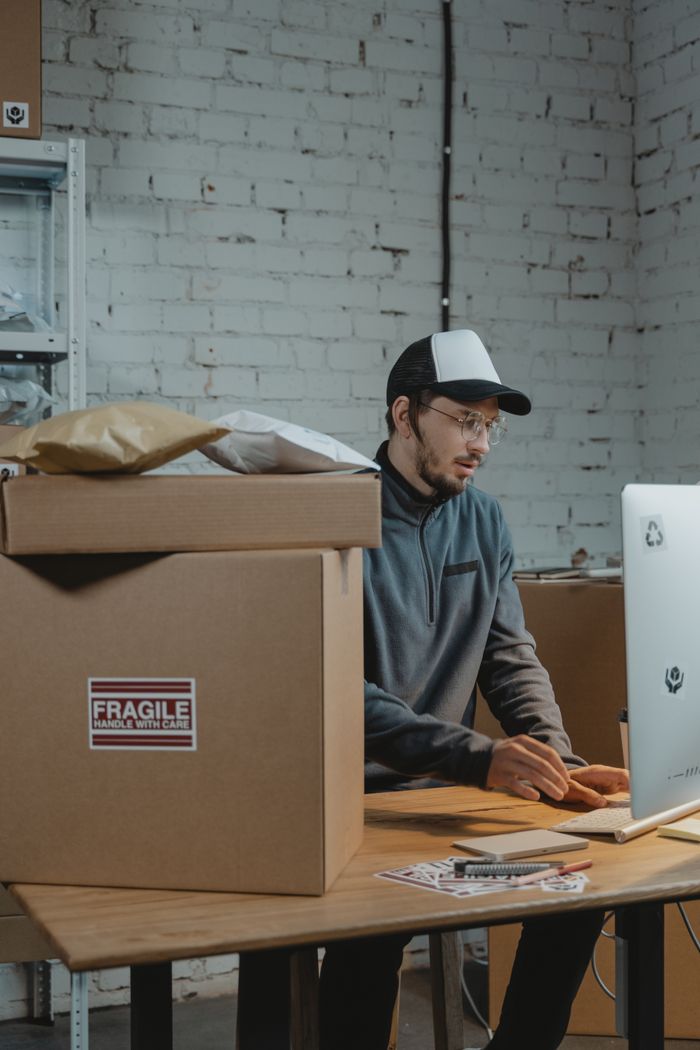 Crafting Captivating Headlines: Your awesome post title goes here Man working on computer in warehouse with packages. E-commerce shipping.