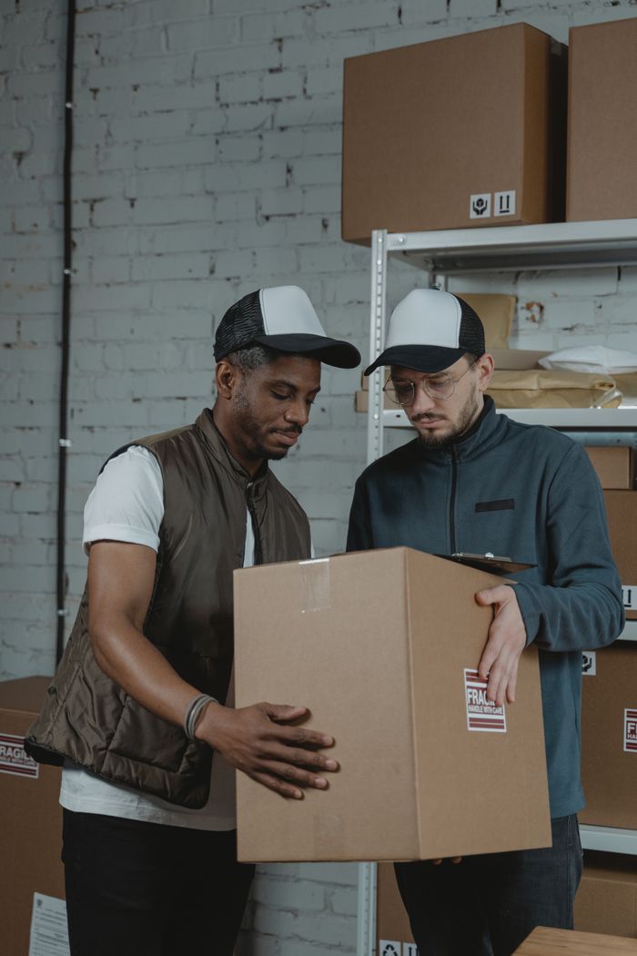 services-img Two diverse colleagues manage a large parcel in a warehouse environment, showcasing teamwork and logistics.