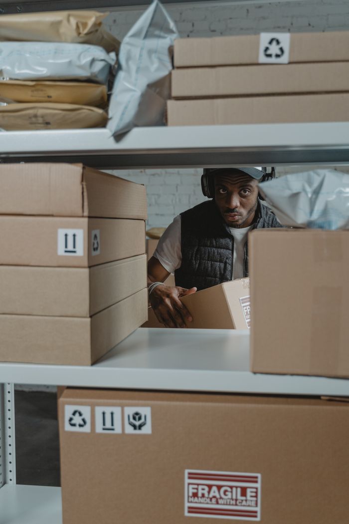 services-01 Man organizing packages on shelves in a warehouse setting with cardboard boxes.
