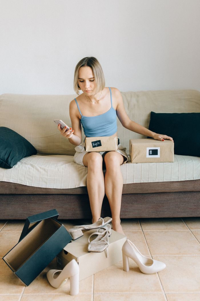 home-img Woman sitting on a sofa with shoes and boxes, shopping online with her phone.